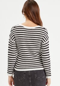 Striped sweater featuring black and white horizontal stripes, knitted texture, and a round neckline. Ribbed cuffs and hem detail.
