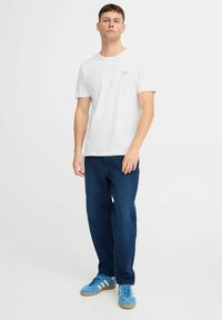 Tricou alb cu mânecă scurtă, cu un mic design grafic pe pieptul stâng, asortat cu blugi largi de culoare bleumarin și încălțări atletice albastre.