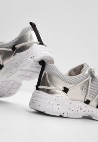 Baskets de sport avec un dessus en argent métallisé, des détails en mesh, des accents noirs et une semelle tachetée de blanc. Design léger et respirant.