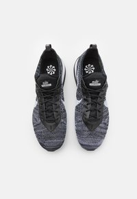 Baskets de sport tricotées noires et grises avec une tige texturée, fermeture à lacets et un logo swoosh blanc sur le côté. Doublure intérieure noire.
