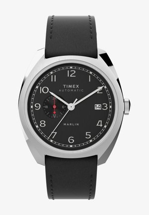 Timex Marlin automatinis laikrodis su juodu ciferblatu, sidabriniu korpusu ir juodu odiniu dirželiu. Ypatybės apima baltus valandų žymeklius ir datos indikatorių.