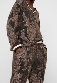 Ensemble de détente marron foncé avec des motifs paisley en rouille et crème, présentant des poignets côtelés et un décolleté en V. Le tissu texturé accentue les détails.