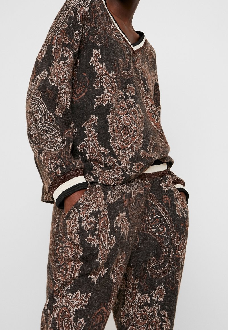Ensemble de détente marron foncé avec des motifs paisley en rouille et crème, présentant des poignets côtelés et un décolleté en V. Le tissu texturé accentue les détails.