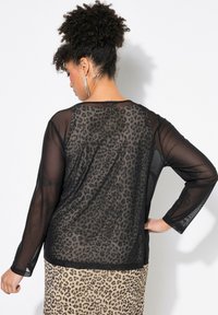 Top nero a maniche lunghe con un corpetto trasparente, schiena con stampa leopardata e scollo arrotondato. Il tessuto è leggero e semi-trasparente.