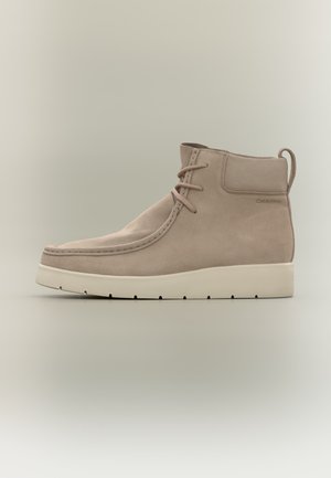 Bottine beige en daim avec semelle blanche, fermeture à lacets, languette latérale et marquage discret Calvin Klein sur le côté.