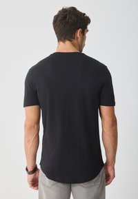 T-shirt preto de manga curta com gola arredondada, feito de algodão. Textura suave com um corte regular, com a barra ligeiramente curvada na parte de trás.