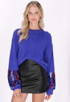 Pull mauve en peluche à manches longues avec des accents de sequins multicolores. Assorti à une mini jupe en cuir noir. Texture douce, design court.