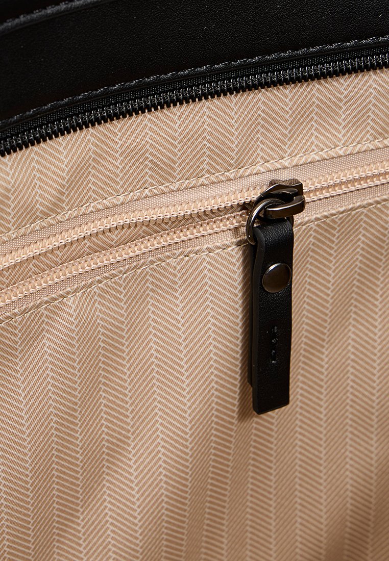 Interno di una borsa caratterizzato da un motivo a spina di pesce color beige e una zip con un tirante in pelle nera. Fodera nera testurizzata nella parte superiore.