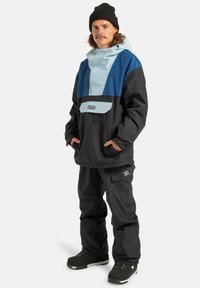Niebieska i czarna ocieplana kurtka z kapturem, posiadająca przednią kieszeń, zestawiona z czarnymi spodniami cargo i czarnymi butami zimowymi. W zestawie ciepła wełniana czapka.