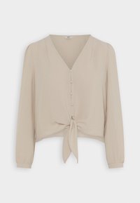 Blouse beige à manches longues avec col en V, boutons recouverts de tissu sur le devant et un nœud noué au bas de l'ourlet.