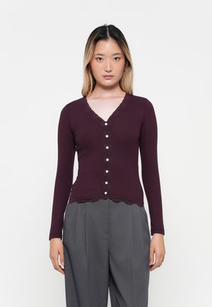 Langermet bordeaux cardigan med v-utringning og blonder detaljer, laget av strukturert stoff og med perleknapper foran, kombinert med grå bukser.