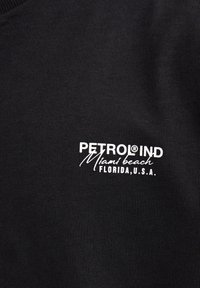 Černé bavlněné tričko s bílým grafickým nápisem: "PETROL® IND Miami Beach FLORIDA, U.S.A." Jednoduchá, žebrovaná textura.
