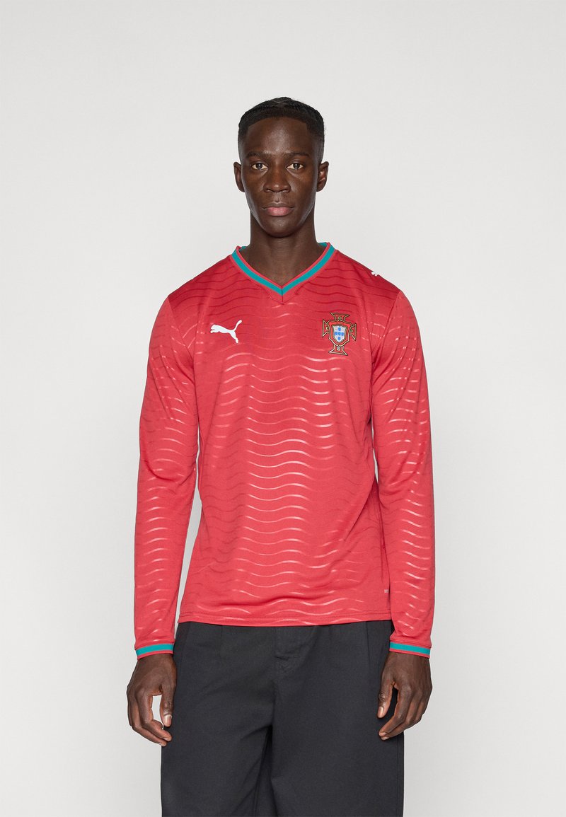 Κόκκινο μακρυμάνικο φανέλα με κυματιστό σχέδιο, αντίθετο τουρκουάζ γιακά και μανσέτες, διαθέτει λογότυπο Puma και έμβλημα της Πορτογαλίας στο στήθος.