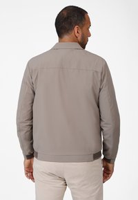 Light brown, smooth fabric bomber jacket with a collar, elastic cuffs, and a textured waistband, viewed from the back, with a simple design.