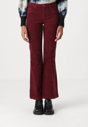 Burgundy corduroy flared pants with prominent vertical stripes, five-pocket design, and fitted waist, paired with black shoes.