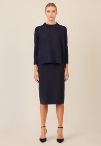Granatowy sweter z prążkowanymi detalami i okrągłym dekoltem, połączony z dopasowaną granatową spódnicą. Oba elementy wykonane są z miękkiego materiału.