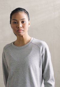 Lys grå sweatshirt med lange ermer, bred halsutskjæring og subtil tekstur. Materialet ser mykt og litt elastisk ut.