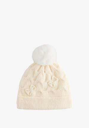Strikket hue i cremet farve med ribbet kant, kabelmønster og to sløjfedetaljer. Afsluttet med en fluffy hvid pompon på toppen.
