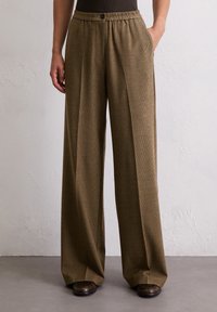 Bruine geruite wijde broek met een elastische tailleband en knoopdetails. De stof is gestructureerd en valt losjes.