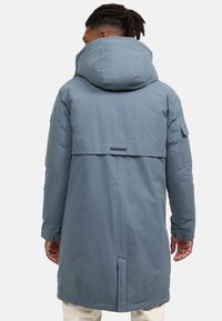 Világoskék, hosszú parkabéléses kabát kapucnival; hátul hajtókával, oldalsó zsebekkel és gombdíszítéssel rendelkezik az ujjakon. Sima textúra.