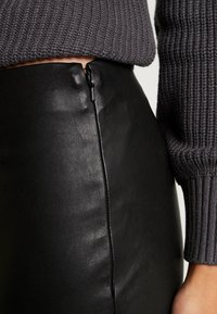 Svart läderkjol med en smidig design, med en synlig dragkedja bak, tillsammans med en texturerad grå stickad tröja.