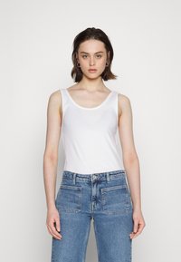 Camiseta branca sem mangas feita de algodão macio, combinada com jeans de cintura alta azul-claro com um design clássico de cinco bolsos.