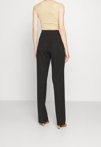 Pantalon noir taille haute avec une coupe ajustée et un devant plat, associé à un haut beige sans manches avec des épaules découpées.