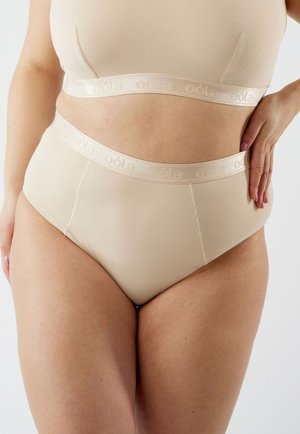 Beige naadloze hoog-waist slip met een zachte elastische tailleband waarop de merknaam "oöla" is gedrukt. Glad, rekbaar stof zonder zichtbare naden.