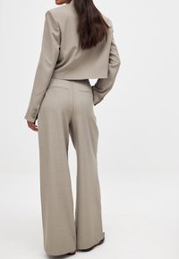 Blazer beige clair cintré avec une fermeture à un bouton, associé à un pantalon large taille haute en tissu assorti et à la coupe ajustée.
