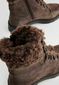 Botas de ante marrón con un collar de textura suave y esponjosa. Cuentan con cierres de cordones y cremallera. Suelas de goma para mayor tracción.