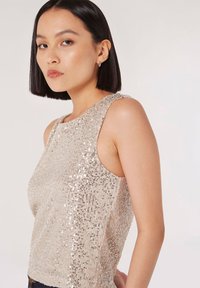 Top senza maniche con un design beige scintillante, caratterizzato da paillettes disposte verticalmente. La texture liscia e la forma aderente esaltano l'aspetto contemporaneo.