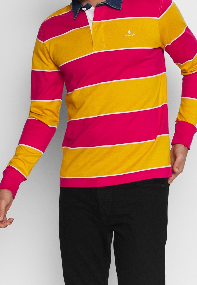 Långärmad polotröja med rosa och gula horisontella ränder och vita detaljer, med en denimkrage och broderad logotyp på bröstet.