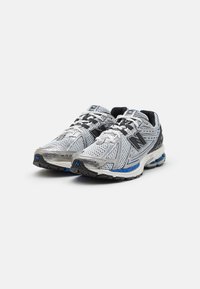 Ett par vita och grå New Balance löparskor med svarta och blå detaljer, vita snören och en andningsbar meshdesign.