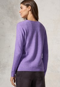 Lilla strikket sweater med lange ærmer, rund halsudskæring og en let løs pasform. Fremstillet af blødt, tekstureret stof. Bæret sammen med mørke bukser.