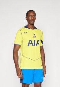 Gul Nike trøje med blå krave, prydet med et stort sort "AIA" logo og klubmærke. Bæres med blå shorts. Stribet tekstur overalt.