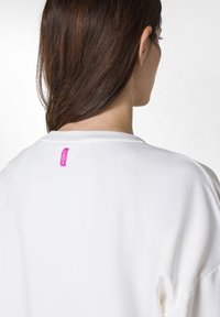 Vit sweatshirt med rund hals och avslappnad passform. Har en liten rosa etikett på baksidan. Slätt tyg med minimala sömmar.