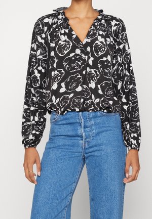 Blusa floreale bianca e nera con scollatura a V, dettaglio di scollatura arricciata, maniche lunghe a palloncino e vestibilità ampia, abbinata a jeans blu a vita alta.
