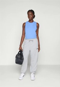 Blå ärmlös sporttopp, grå sweatpants med elastisk midja, vita sneakers och en svart gymväska med vit text.