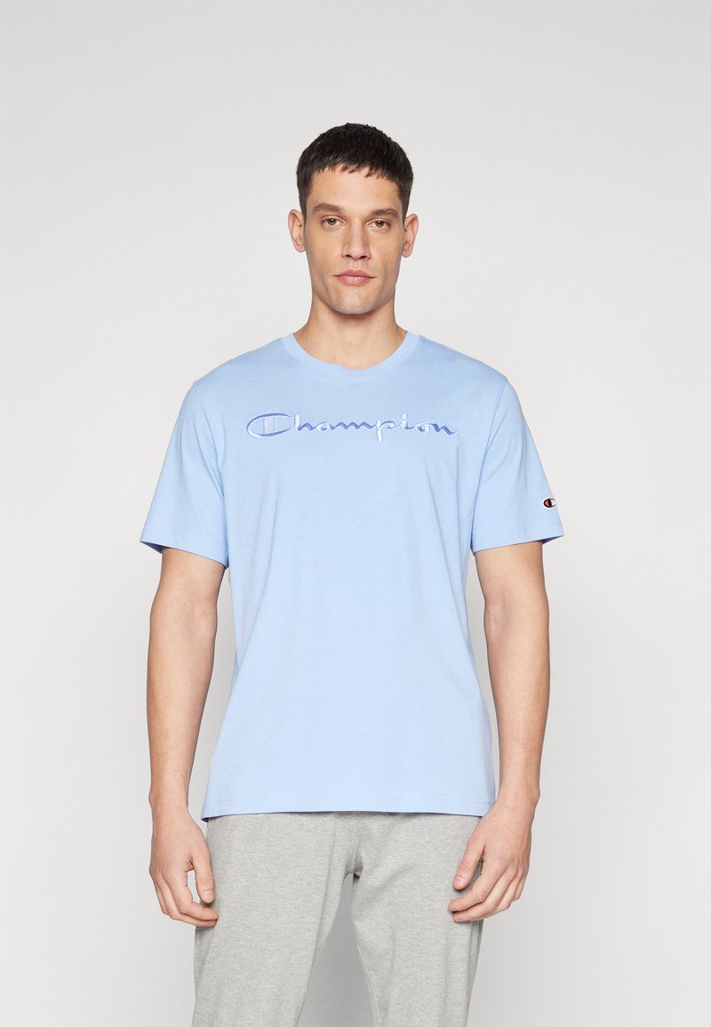 Hellblaues Baumwoll-T-Shirt mit kurzen Ärmeln, das ein gesticktes "Champion"-Logo in einer dunkleren Farbe und ein kleines Logo-Detail am Ärmel aufweist.