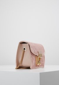 Rosa sammetshandväska med klaffstängning, guldfärgade detaljer, kedjesnodd och en slät läderinredning. Texturerad utsida med en elegant design.