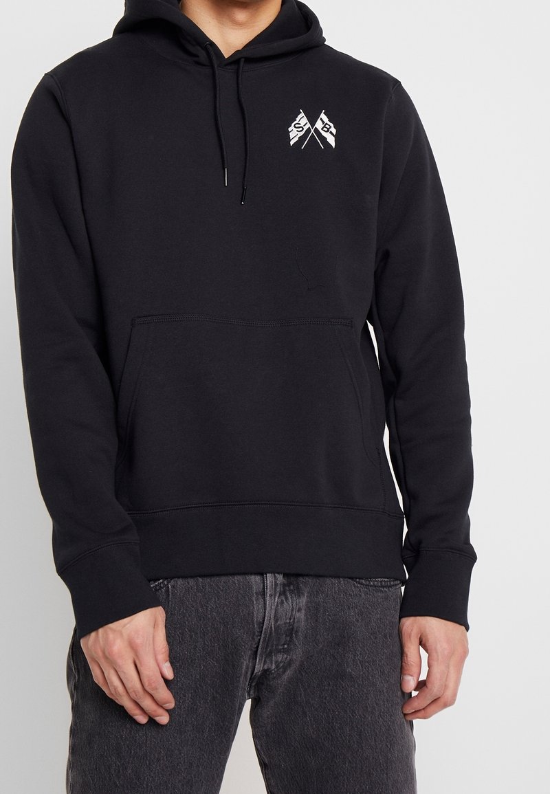 Svart hoodie i bomullsblandning, med en frampocket, ribbad ärmslut och en liten grafisk bild av korsade flaggor på bröstet.