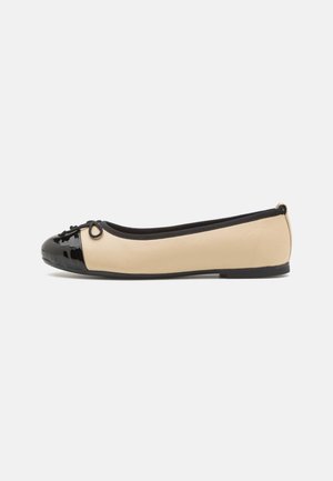 Ballettflats med en beige lærkropp og en blank svart lakkedetail på tåen. Har en liten sløyfe foran. Flatt såle.