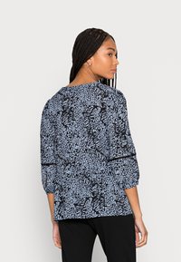 Blusa preta com um padrão abstrato azul, mangas até o cotovelo e um corte descontraído. Apresenta um detalhe franzido nas costas.