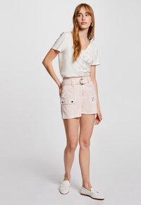 Light pink shorts with two front pockets, a belted waist, and a textured finish, worn with a white V-neck t-shirt and white loafers.