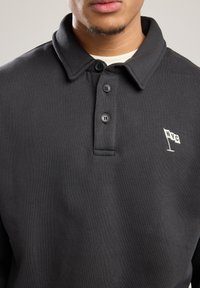 Black cotton polo shirt with a structured collar, three-button placket, and a white embroidered NYC flag logo on the left chest.