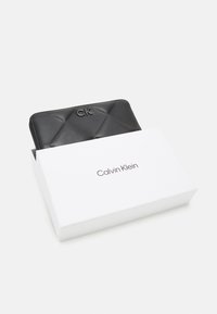 Black quilted leather wallet with embossed "CK" logo, presented in a white box featuring the "Calvin Klein" logo in black.