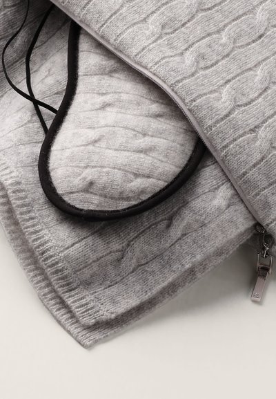 Grå stickad filt med ett kabelmönster, som visar en mjuk, texturerad yta och en kontrasterande svart blixtlåsdetalj som delvis avslöjar ett isolerat fyllmedel.
