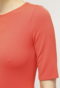 Koraltexturerad topp med korta ärmar. Har en rund halsringning och en figursydd design, som framhäver ett mjukt, elastiskt tyg.