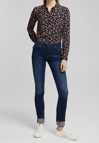Svart skjorta med blommönster och långa ärmar, tillsammans med mörkblå slim-fit jeans och vita sneakers.