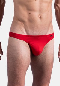 Rote Männerbikini-Briefs mit gerippter Textur, einem glatten Bündchen und minimaler Abdeckung. Mit einem kleinen Markenetikett an der Seite.